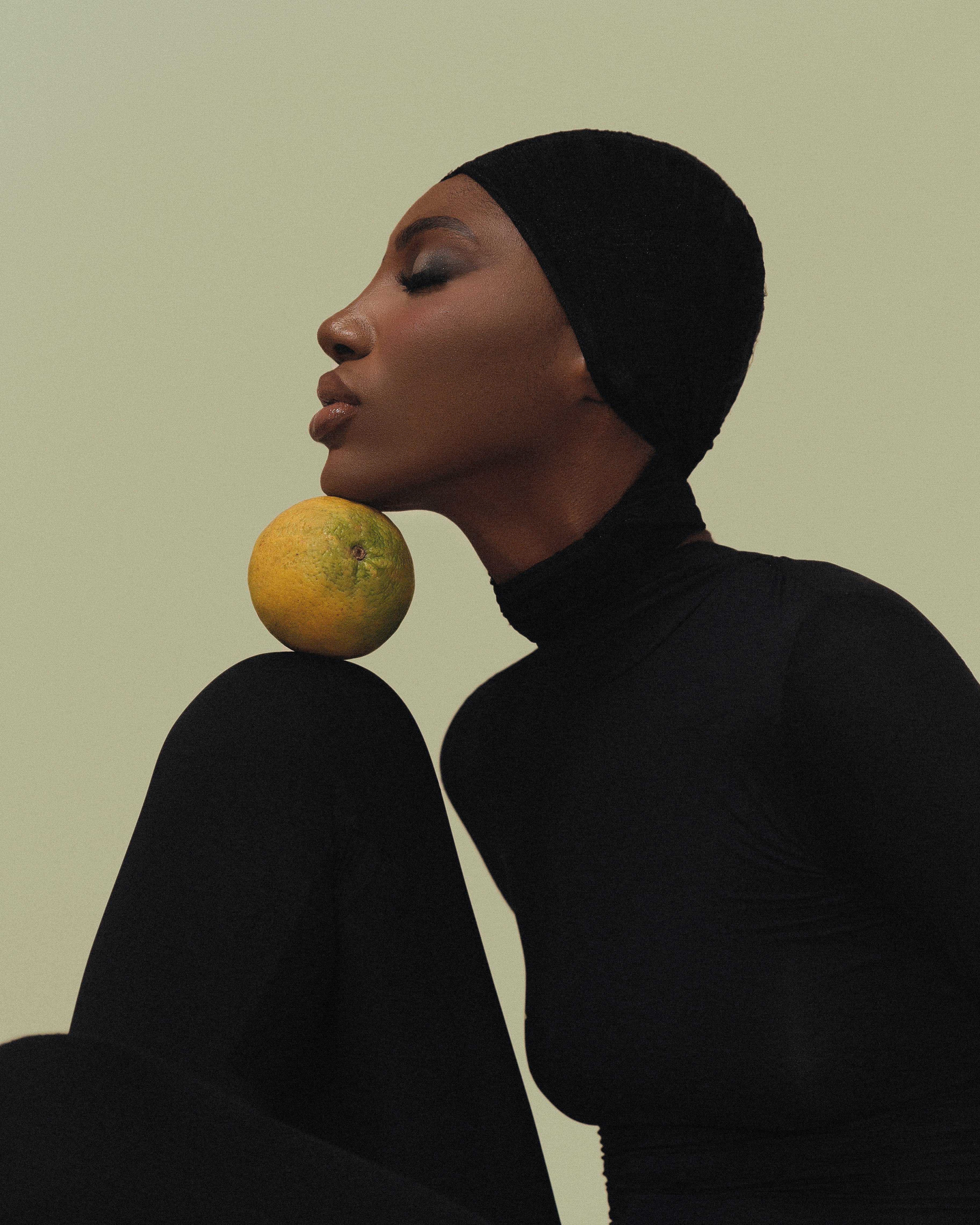 Artistic portrait of a woman balancing an orange on her knee in minimalistic style.
