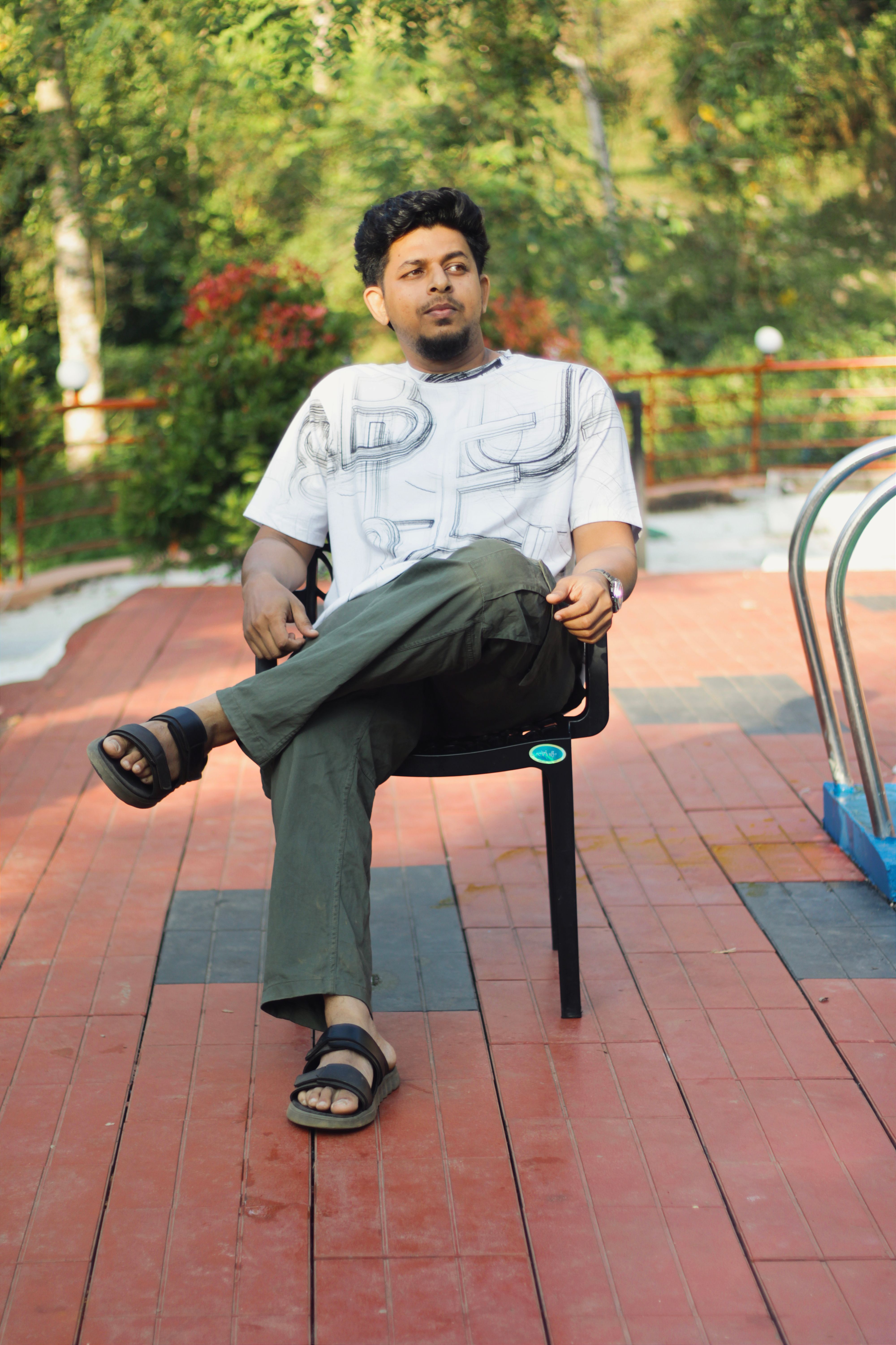 Young man sitting relaxed by a swimming pool in Kakkadampoyil, India. Serene outdoor setting.