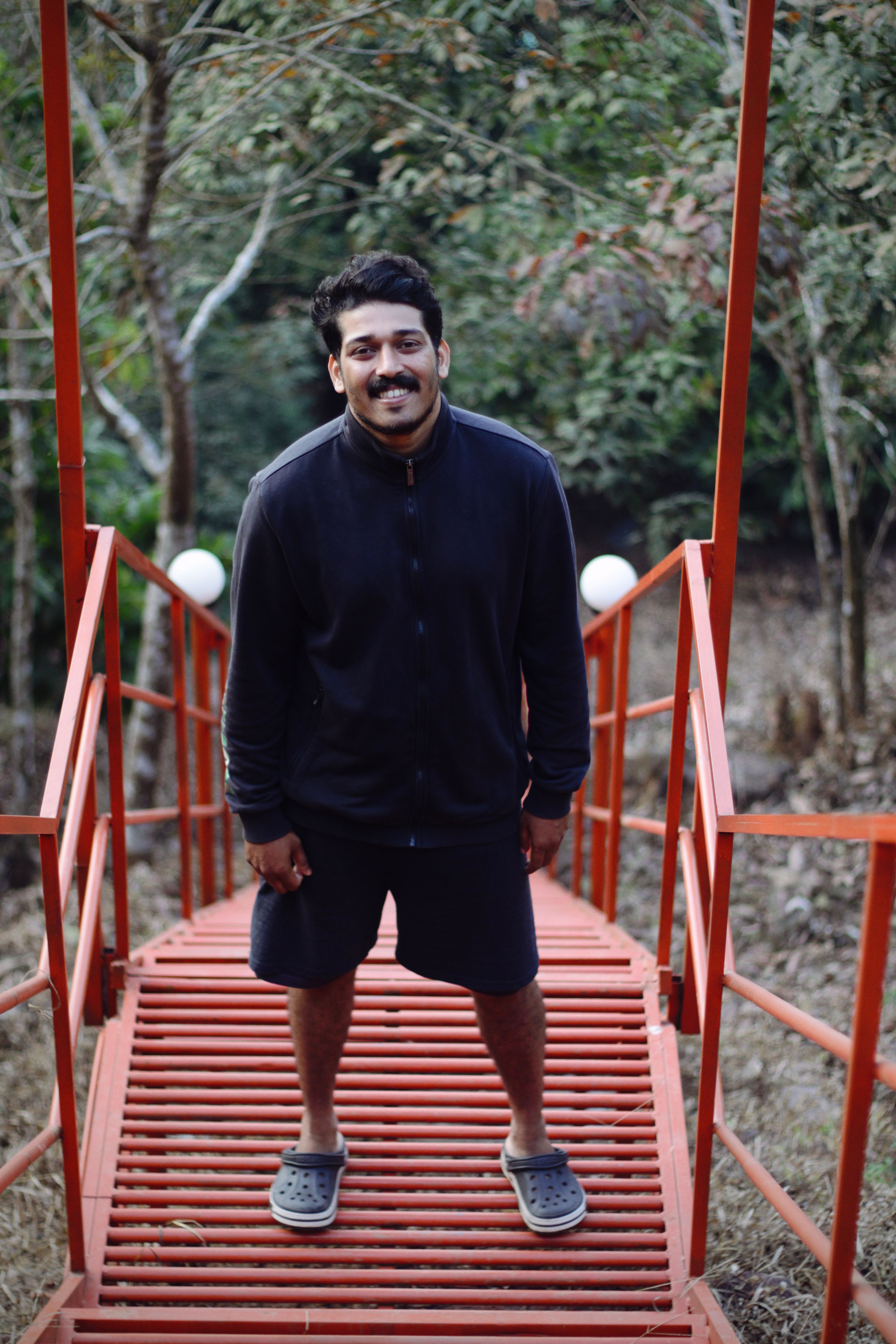 Portrait of a young man on a vibrant red bridge surrounded by nature.