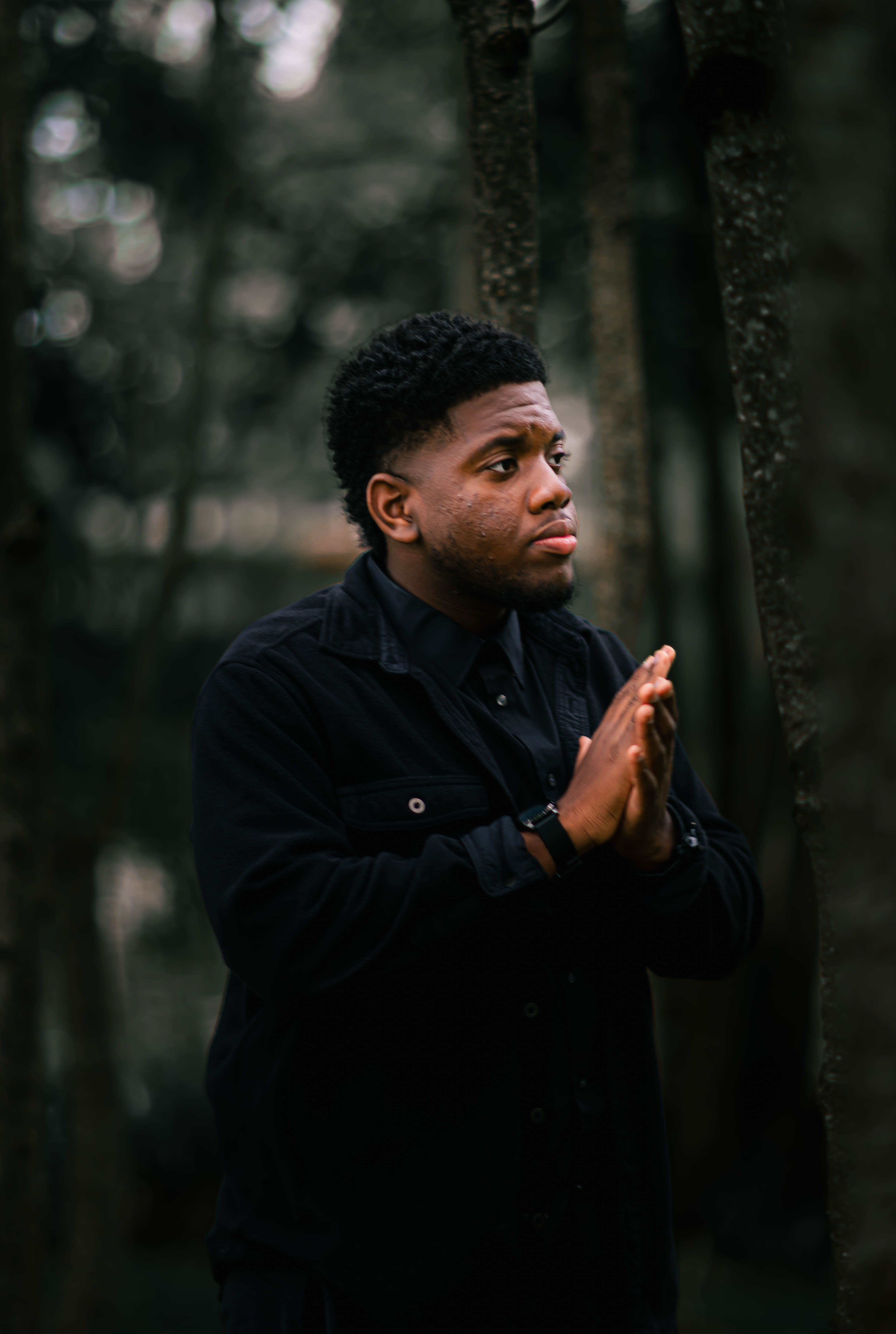 Portrait of a man in deep thought in a forest, surrounded by trees.