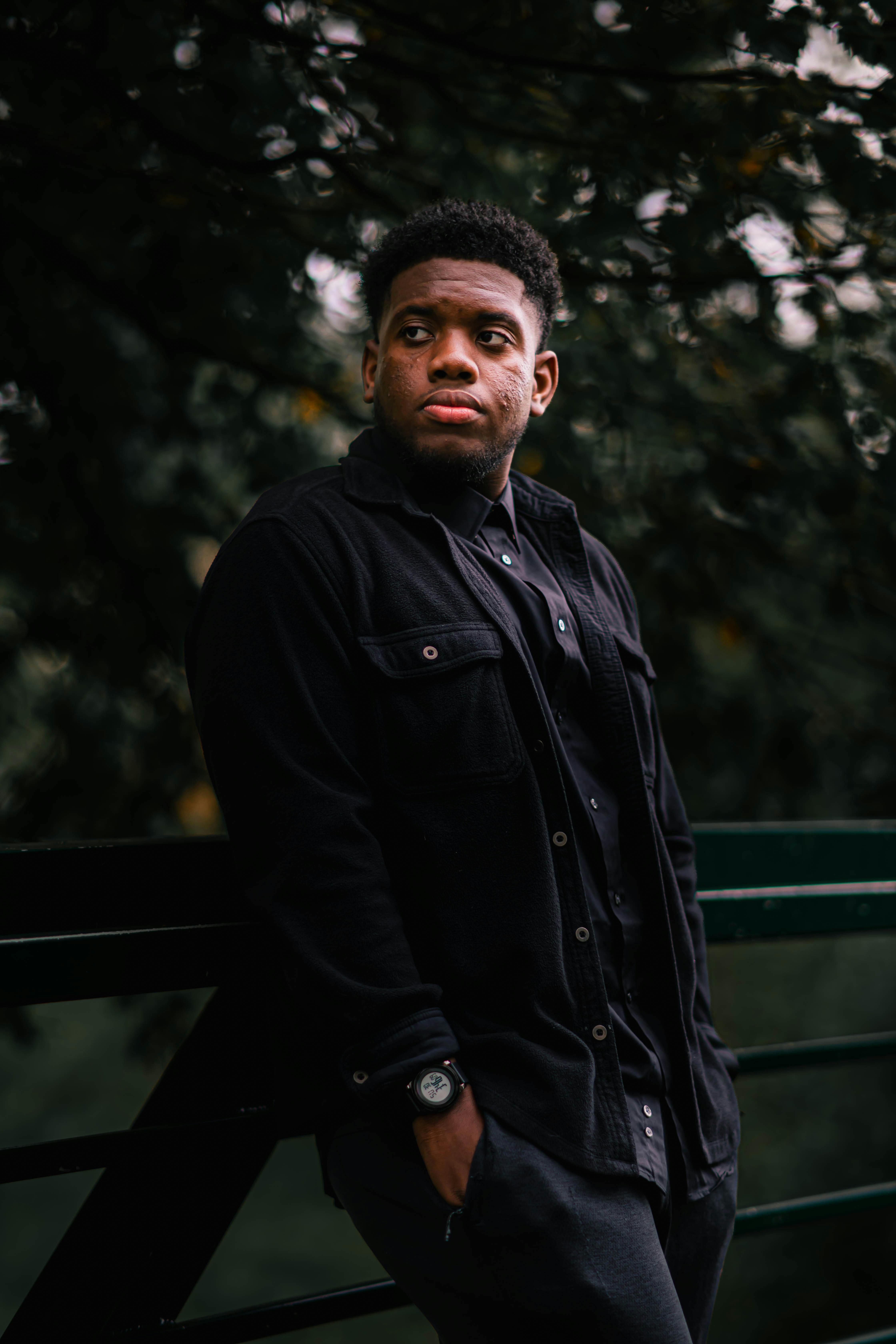 Thoughtful young man leaning on railing in a lush, green park setting.