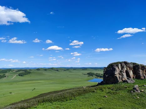 Une vue imprenable sur de vastes prairies sous un ciel bleu vif, avec un affleurement rocheux accidenté.