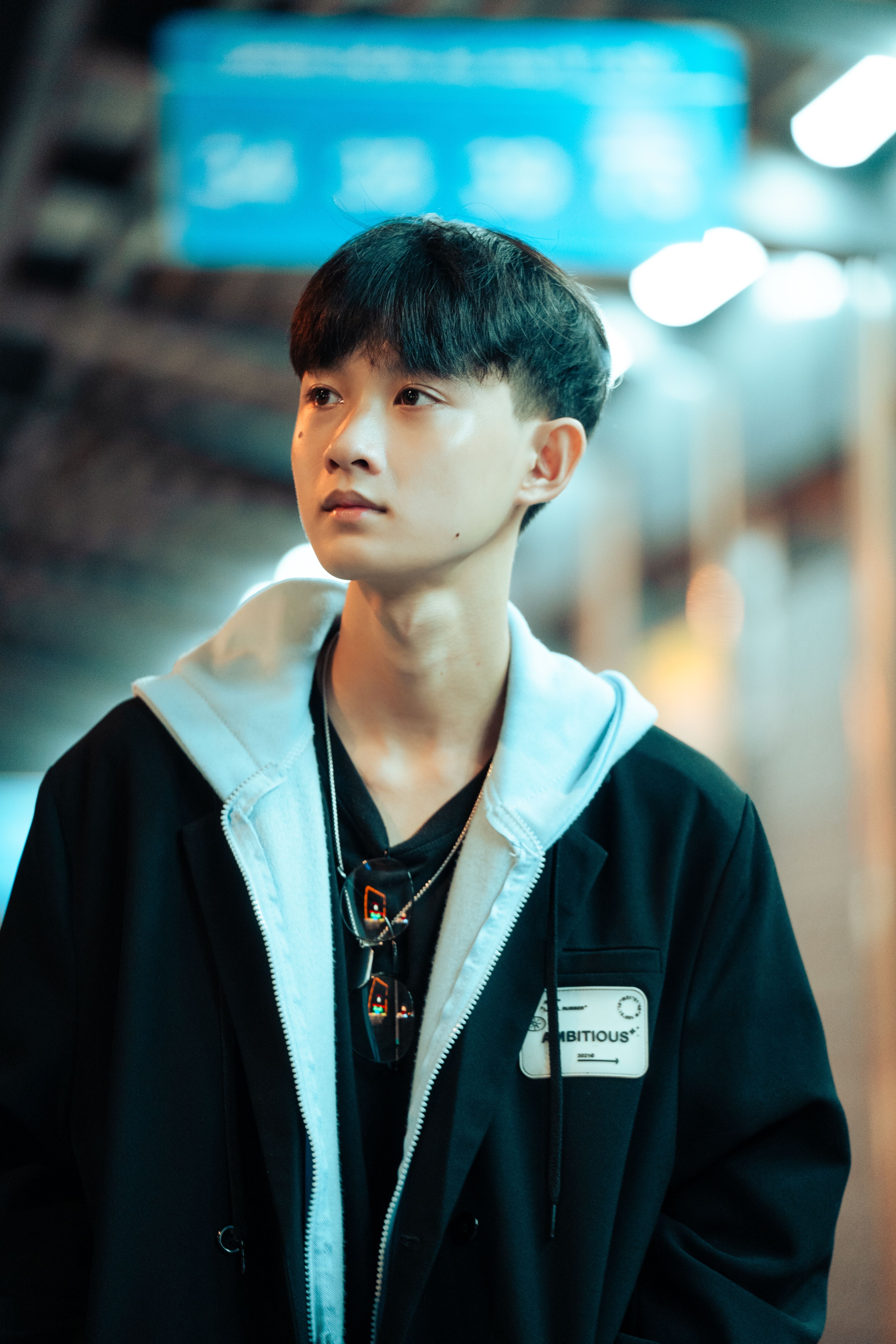 A teenage boy looks thoughtfully away, standing in a blurred urban background at night.