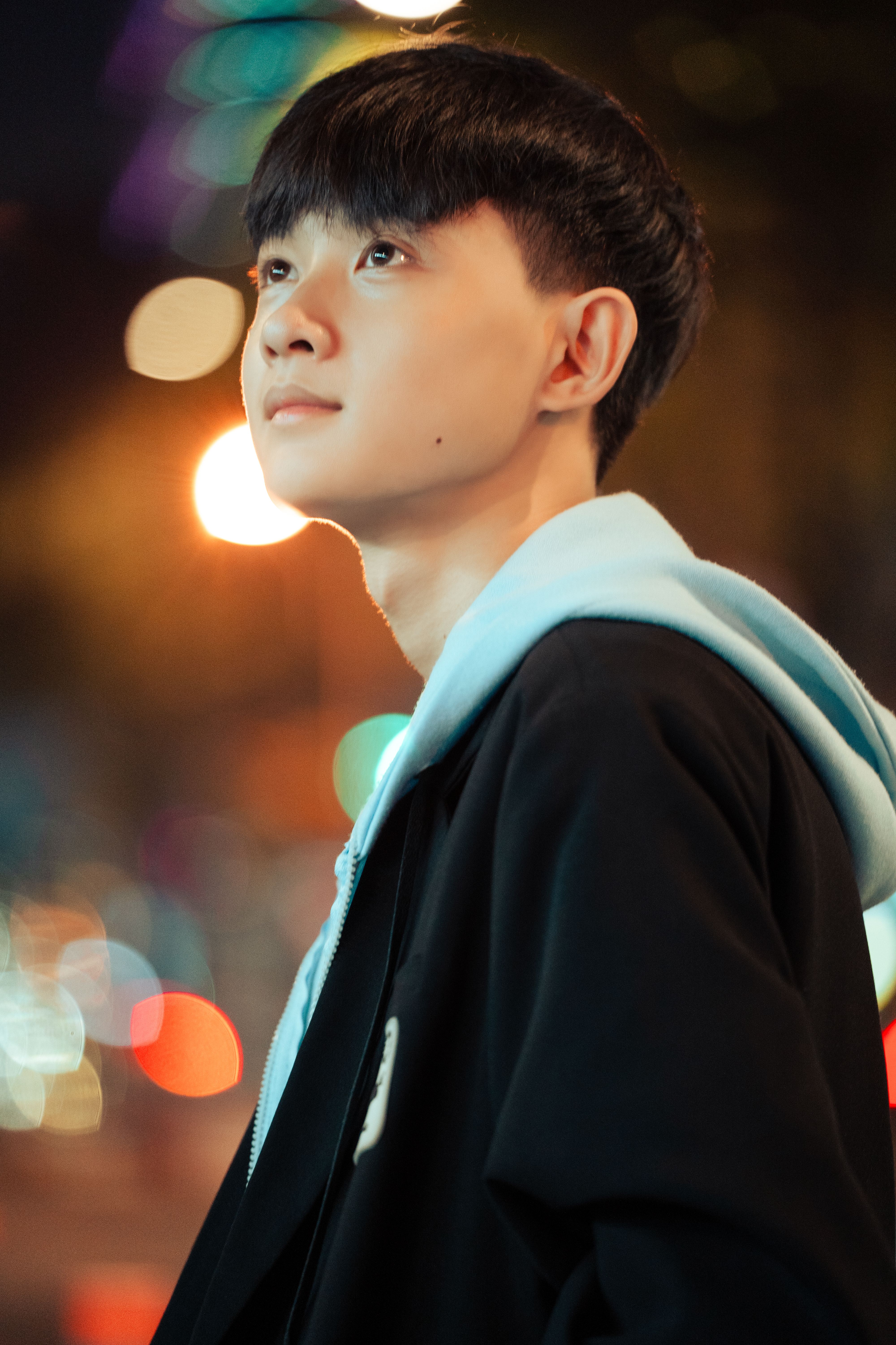A thoughtful young man gazes upward amidst vibrant city lights at night.