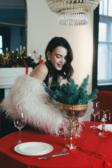 A woman in elegant attire sets a Christmas-themed dining table with festive decorations.