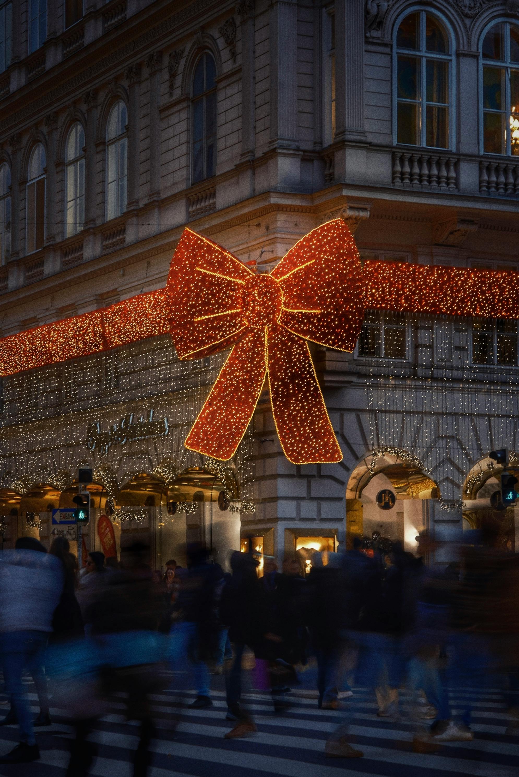 Crowds bustling under large illuminated bow and lights in Vienna during Christmas.