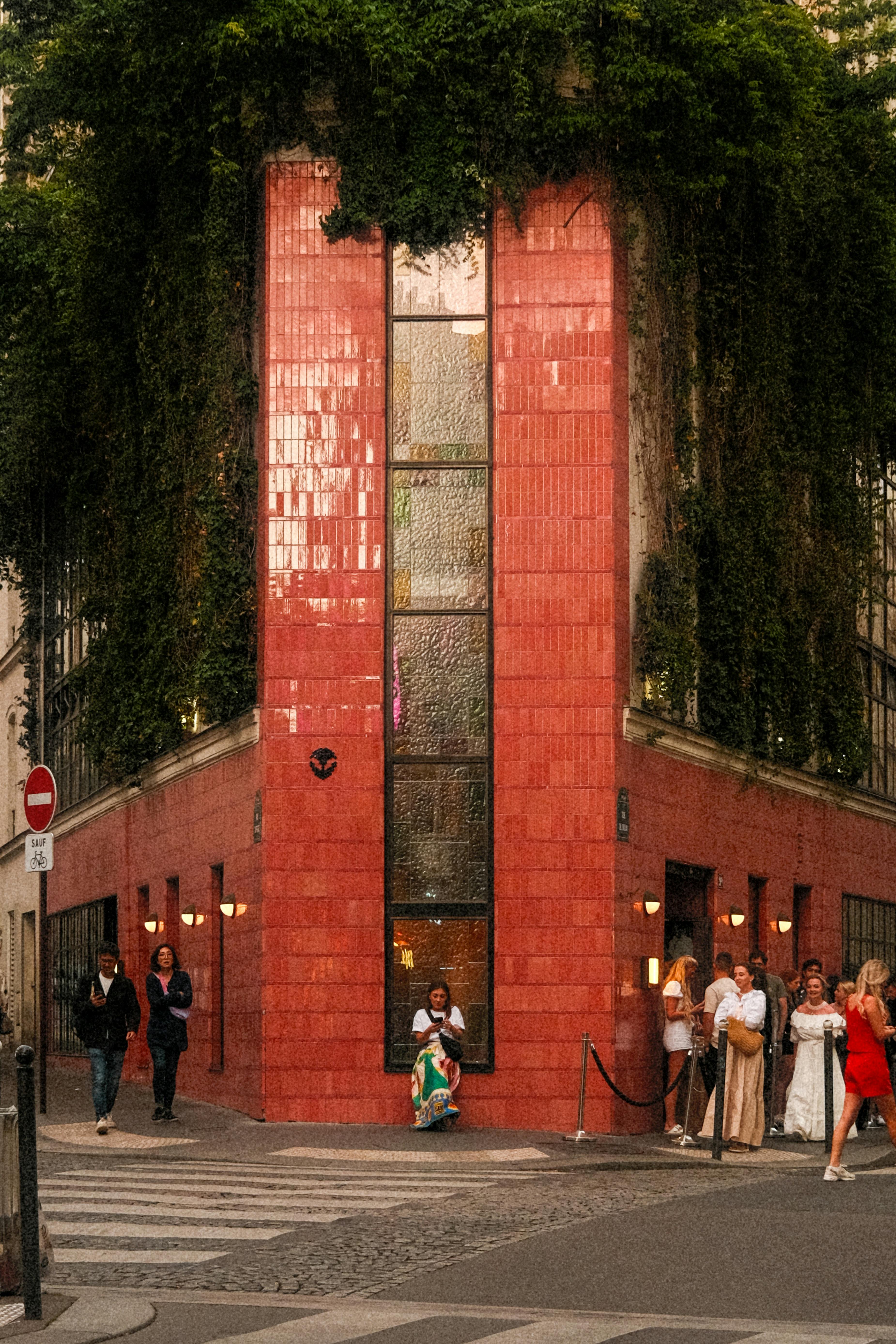 A vibrant red brick building on a lively street corner with lush greenery.