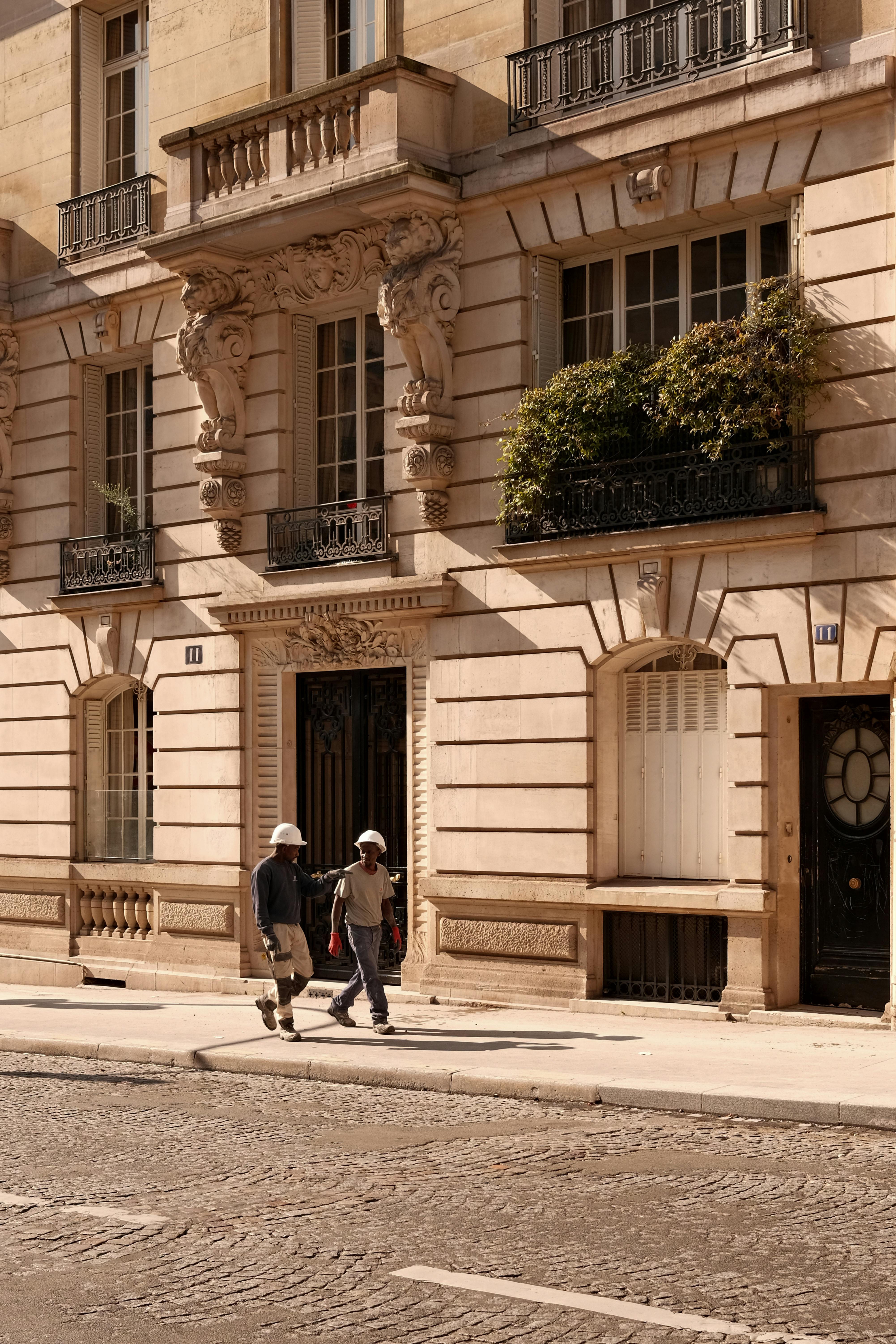 Two people walking by classic Parisian architecture on a sunny day.