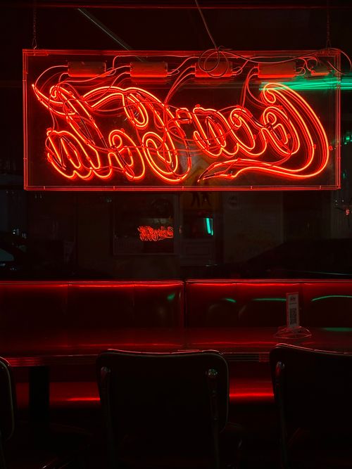 Free Atmospheric shot of a classic diner interior with a glowing red Coca-Cola neon sign at night. Stock Photo