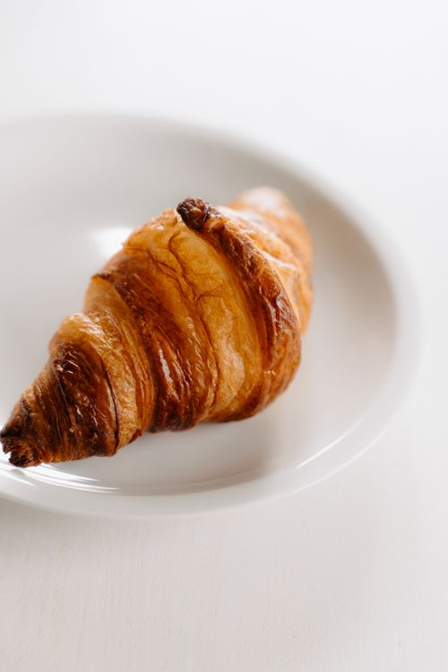 Free Delicious buttery croissant on a white plate, perfect for breakfast inspiration or minimalist food design. Stock Photo