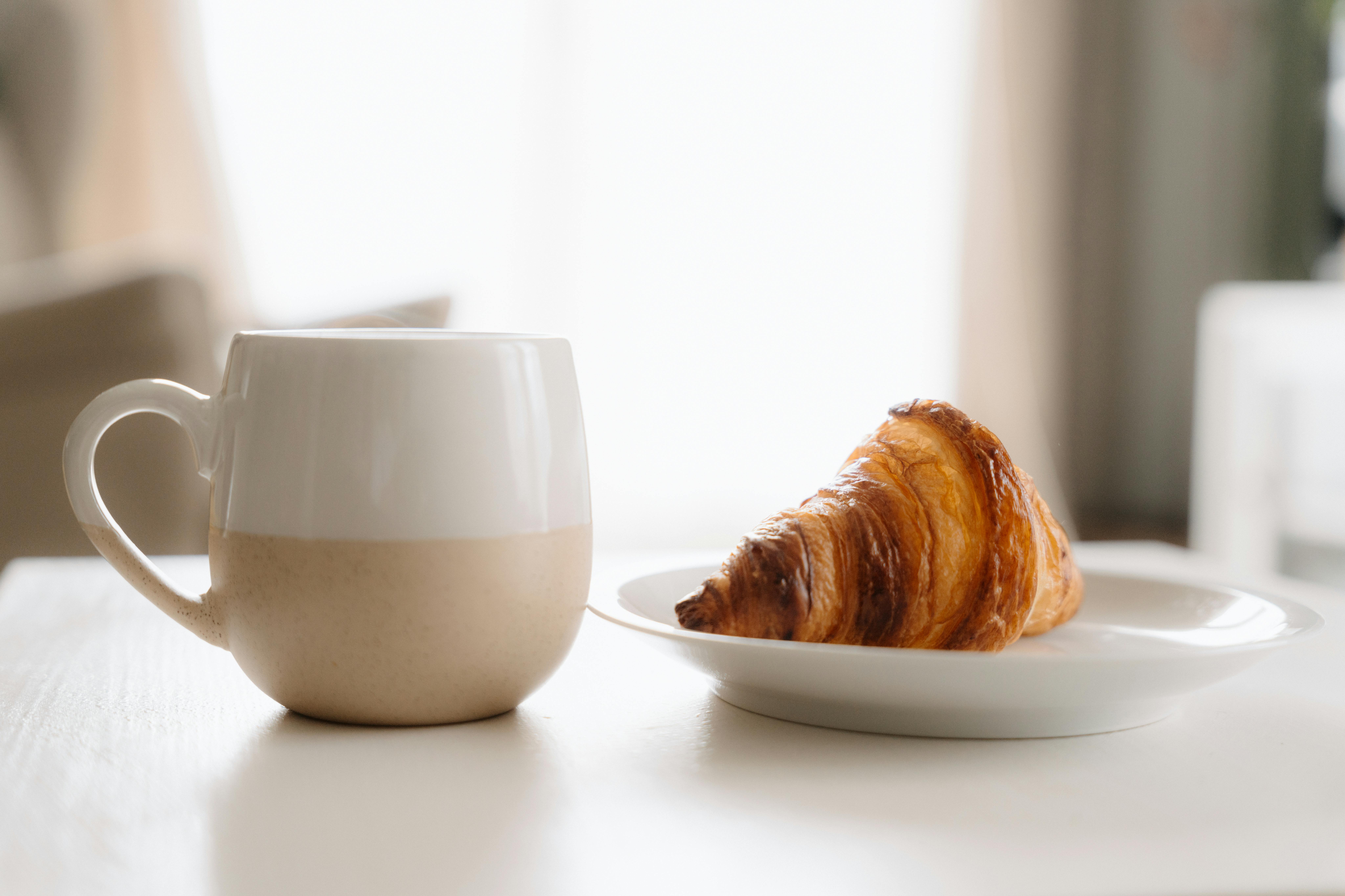 A cup of coffee and croissant on a table, perfect for a cozy morning.
