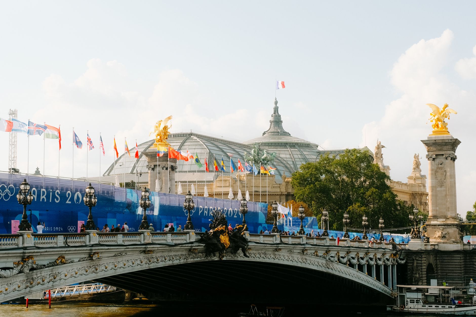 Majestic Parisian scene featuring Grand Palais and Pont Alexandre III during daylight with Paris 2024 banners.