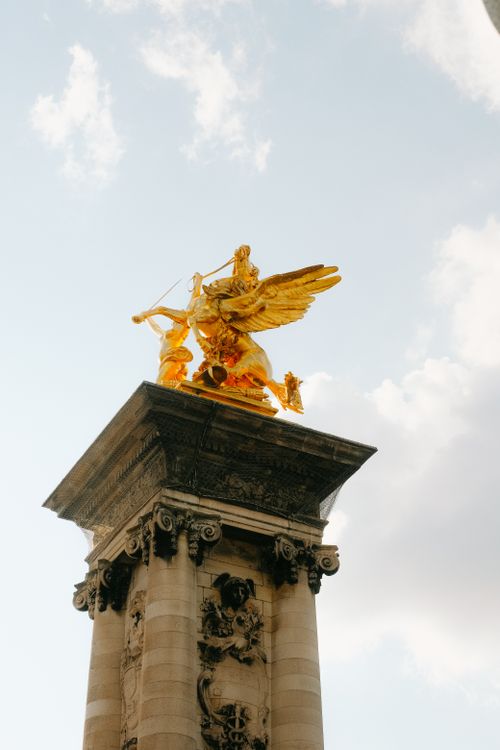 Free View of the golden sculpture atop Pont Alexandre III in Paris under a bright sky. Stock Photo