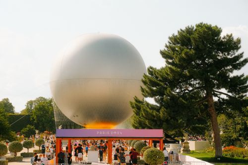 Free A vibrant crowd gathers at a Paris 2024 event with a unique metallic sphere sculpture. Stock Photo