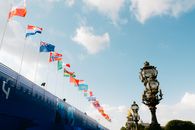 Colorful flags waving against a blue sky next to ornate lamp posts in Paris, France.