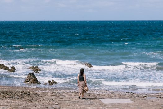 A woman stands on Bude beach in England, admiring the wavy seascape with scattered rocks.