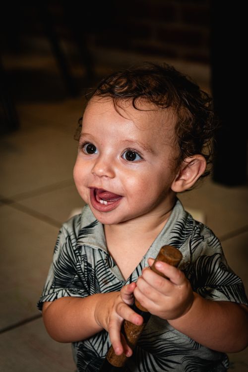 Free A cute baby with curly hair laughs while holding a small brown toy indoors. Stock Photo