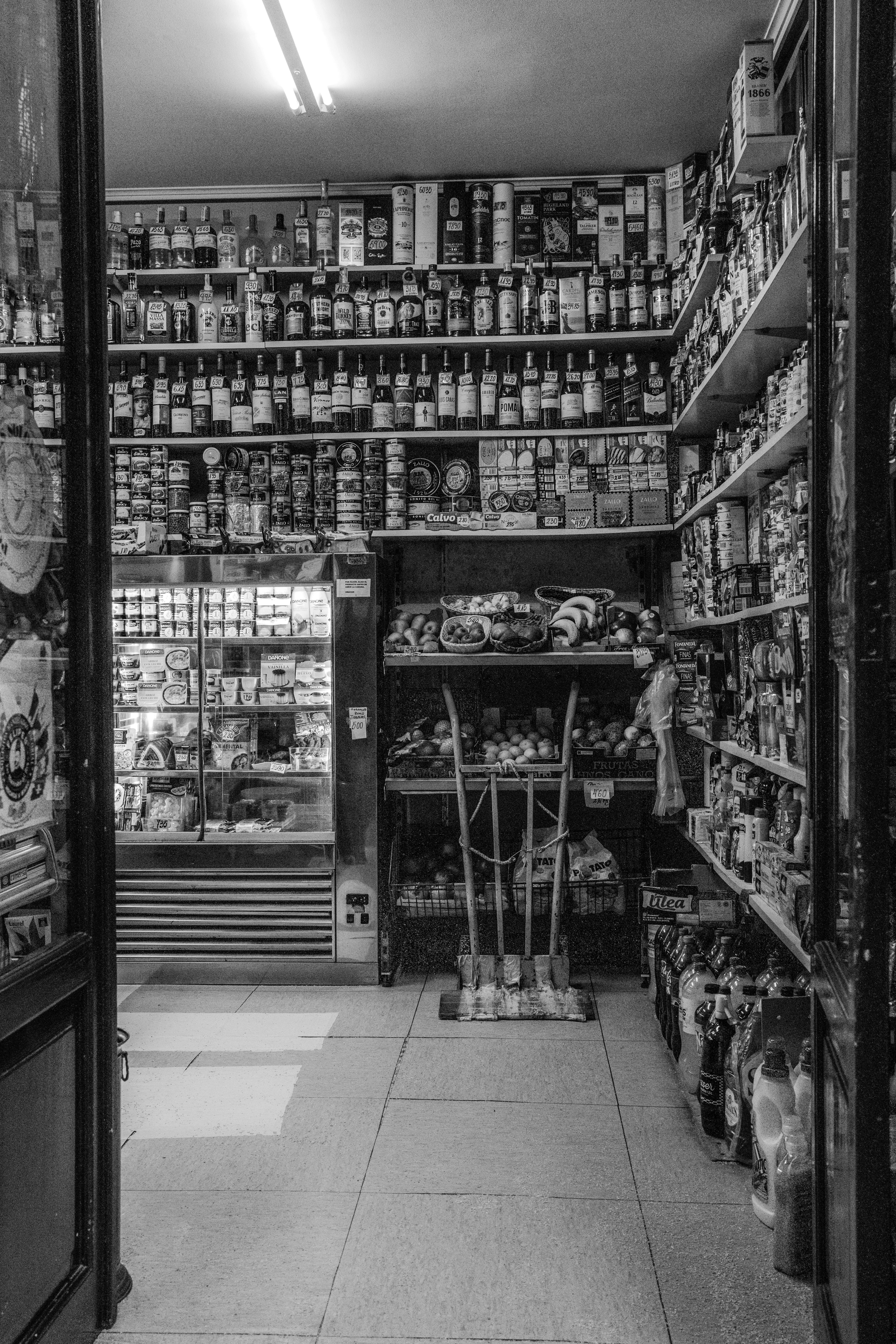 Foto a preto e branco do interior desordenado de uma mercearia cheia de vários produtos.