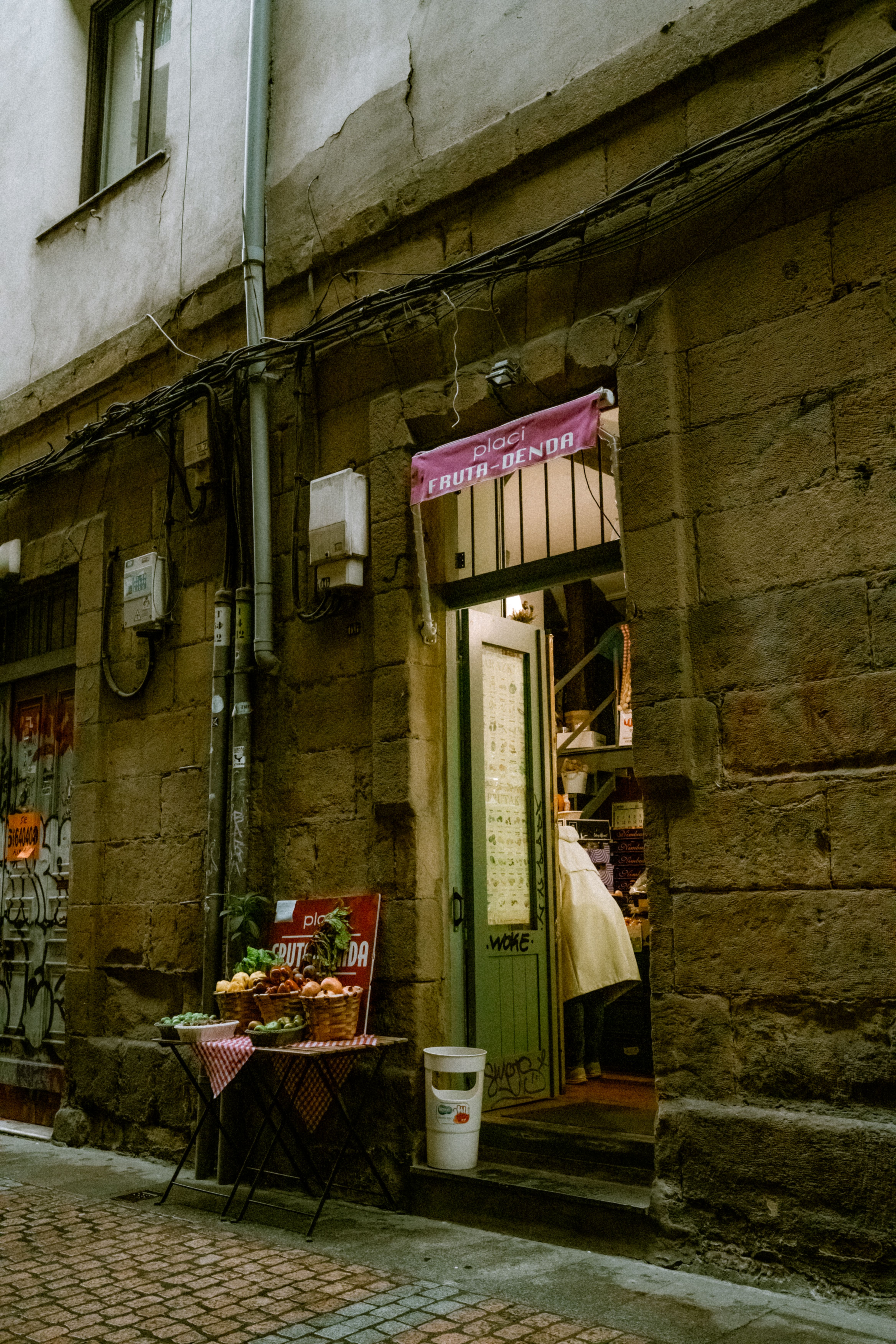 Fotomural Una acogedora entrada de frutería en un estrecho callejón histórico de adoquines con una mesa de frutas expuesta.