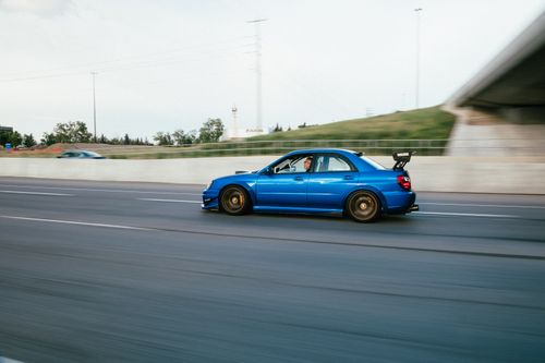 Free A blue modified Subaru STI driving fast on a highway, showcasing speed and performance. Stock Photo