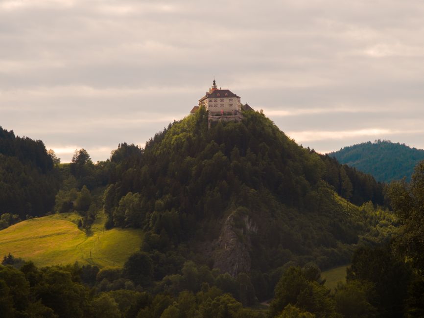 A breathtaking view of an Austrian castle perched atop a green hill surrounded by forests and landscape.