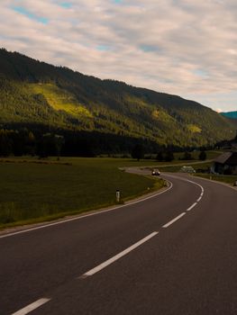 Curving road in Rakúsko under a dramatic evening sky and lush green mountains.