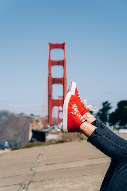 A person wearing red sneakers relaxes with the Golden Gate Bridge in the background.