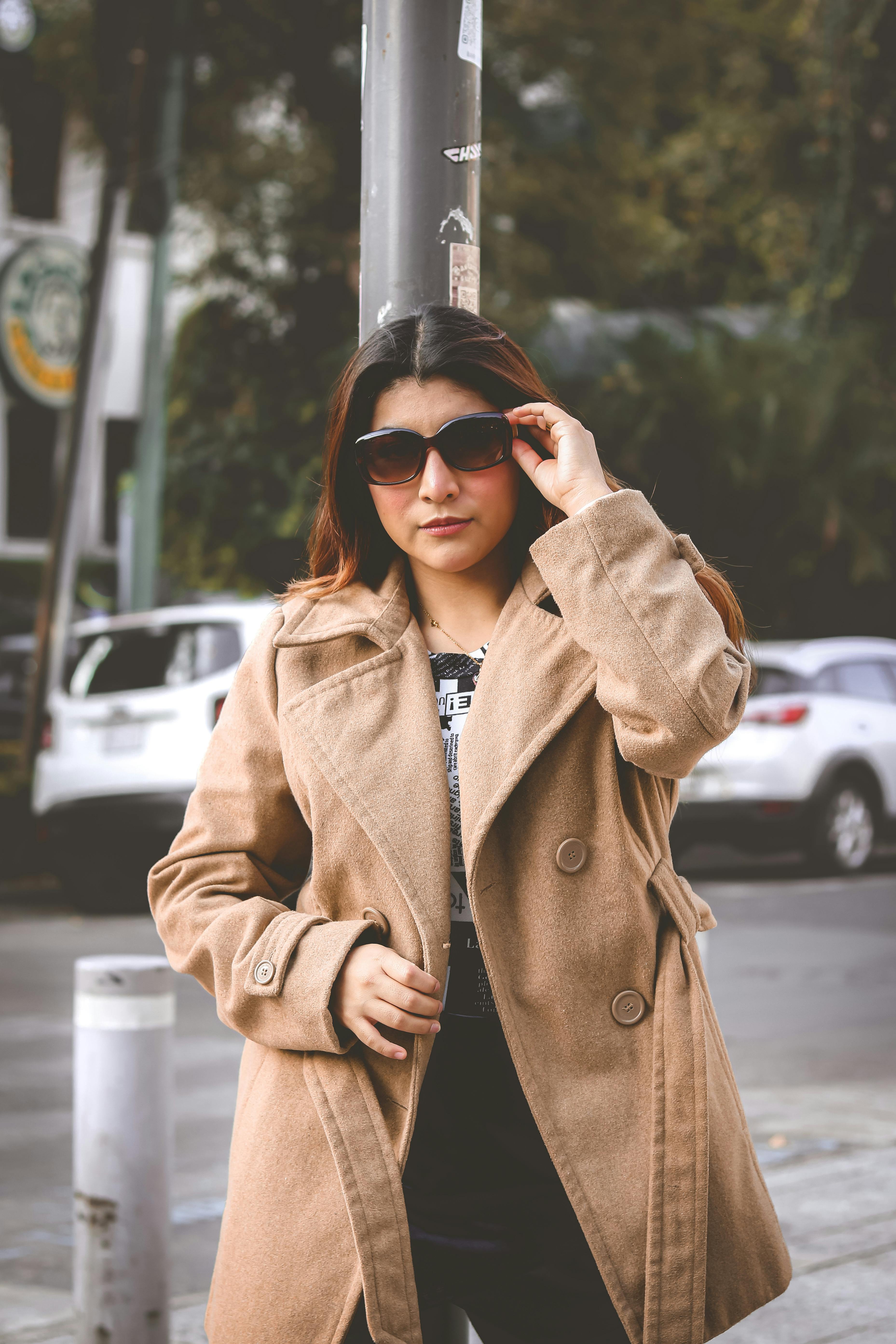 Fashionable woman wearing a brown coat and sunglasses on an urban street.