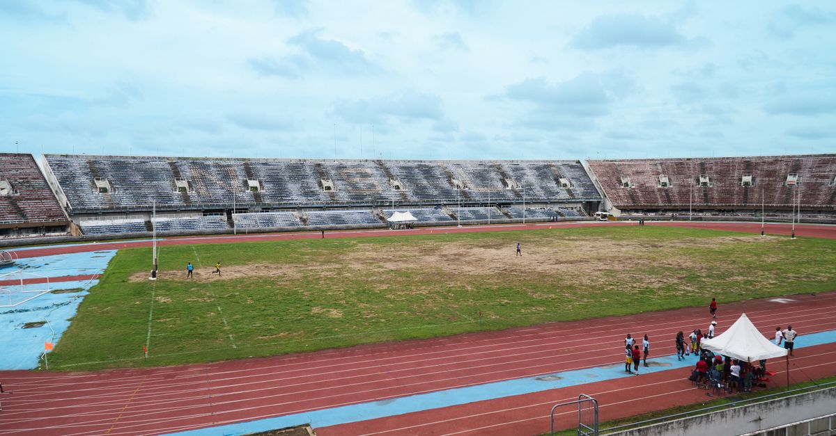 A spacious outdoor stadium with an empty field and surrounding running track under a cloudy sky.