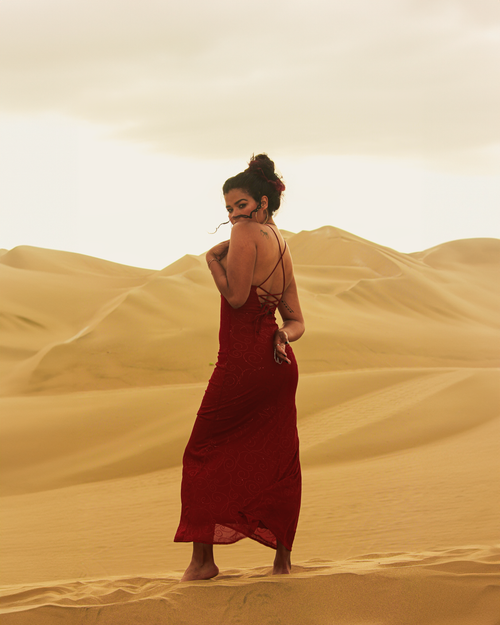 Free A woman in a red dress poses gracefully in vast desert dunes under cloudy skies. Stock Photo