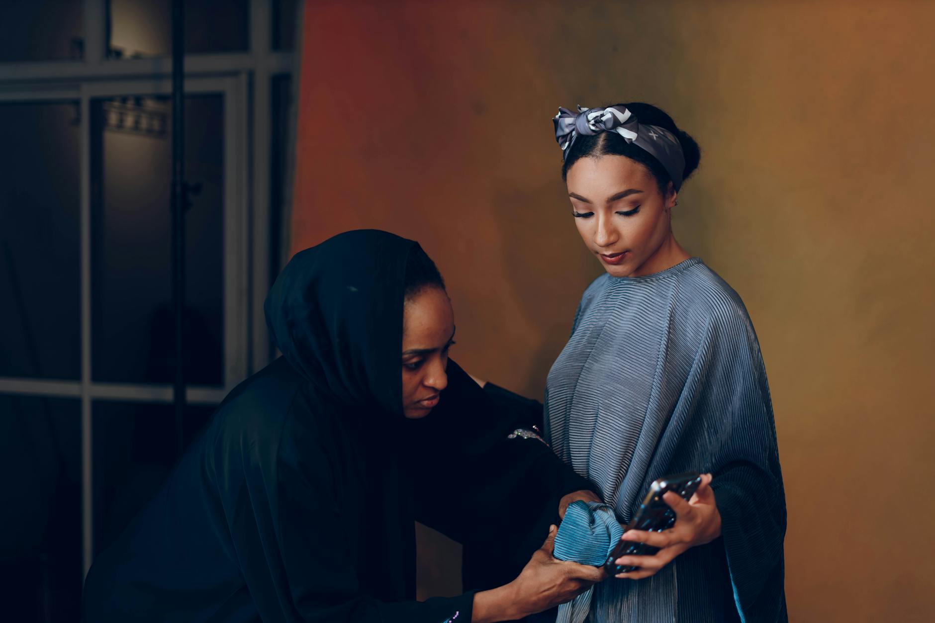 Model and designer collaborate during a fashion styling session indoors, showcasing a blue dress.
