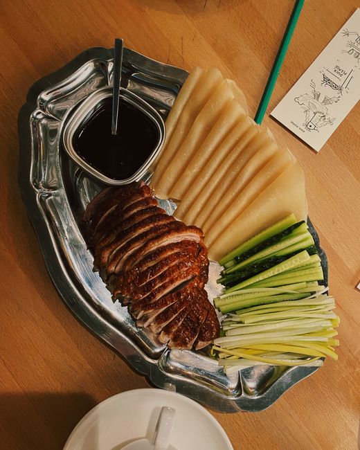 A platter of shredded stir-fried moo shu chicken with cabbage, egg, and mushrooms next to a stack of thin pancakes and a bowl of hoisin sauce