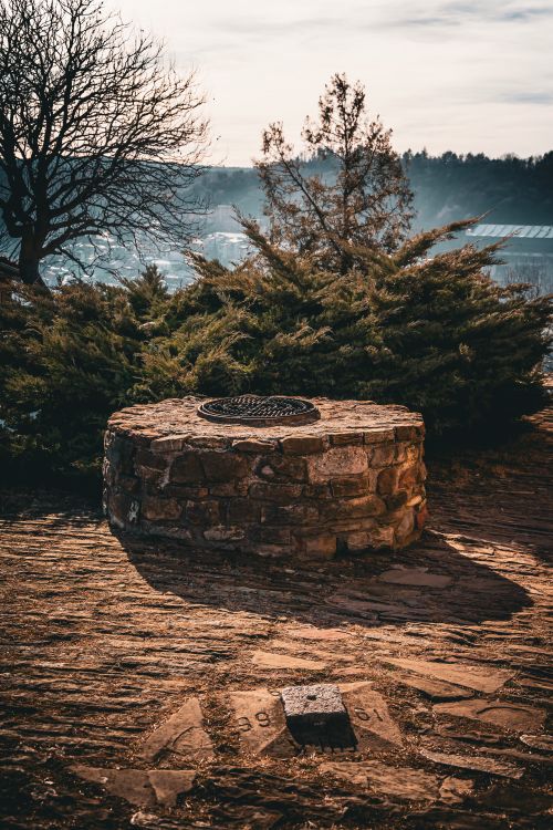 Free A vintage stone well in the outdoors under warm sunlight with trees and hills. Stock Photo