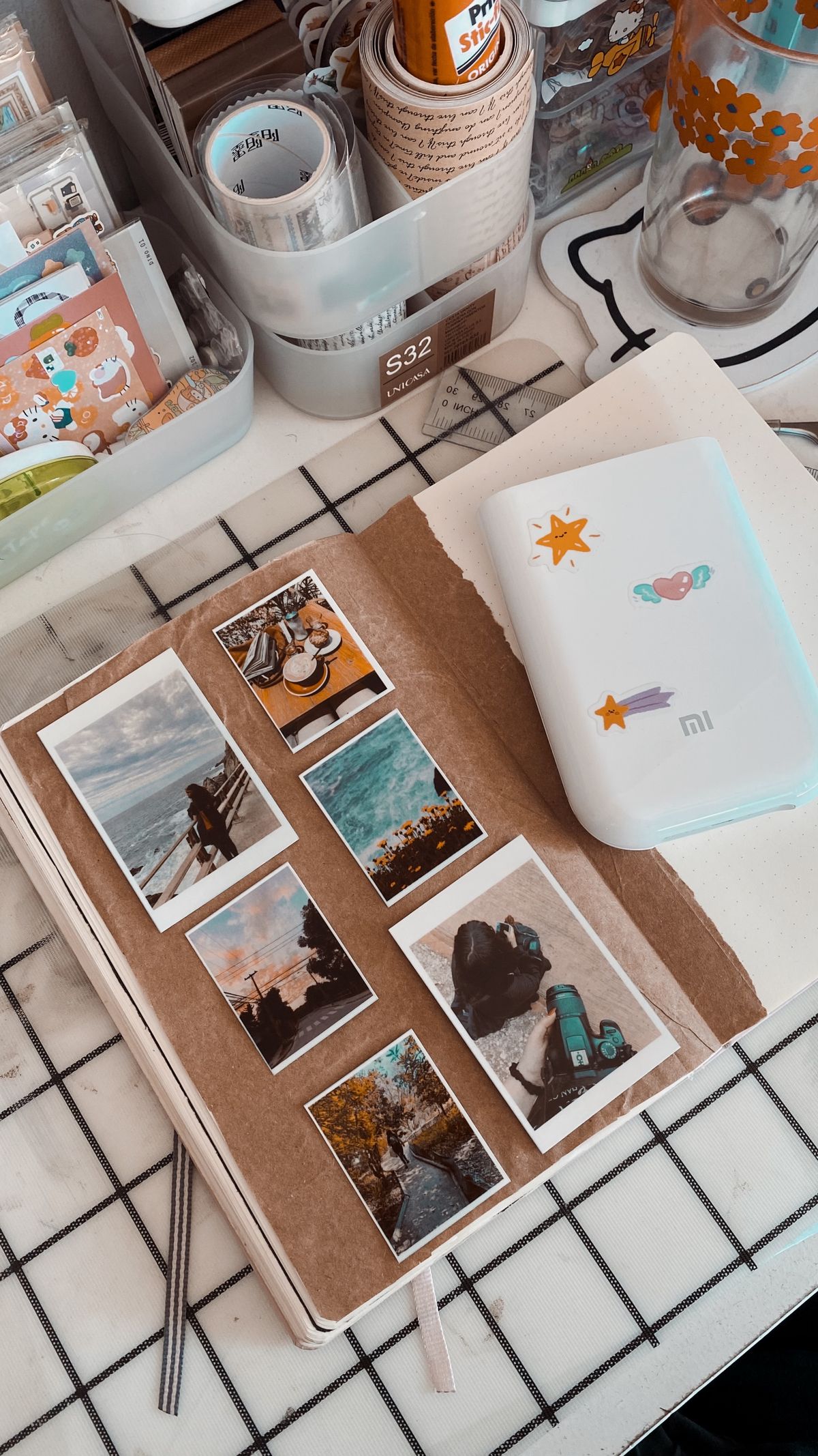 An open paper travel journal beside printed photographs, laid out on a desk.