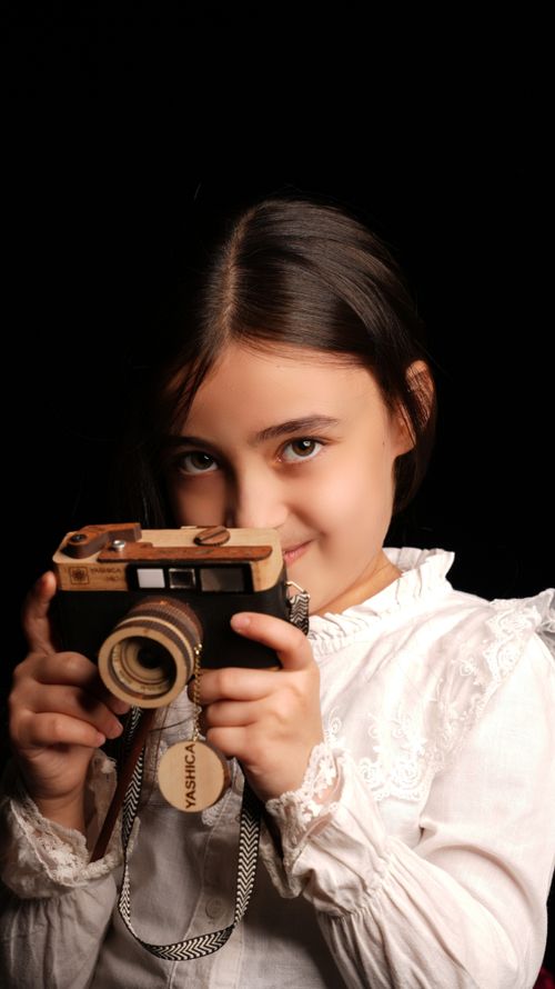 Free Child smiling while holding a vintage camera, against a dark background. Stock Photo