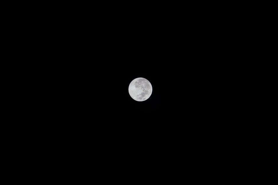 A clear view of the full moon against a dark, starless night sky.