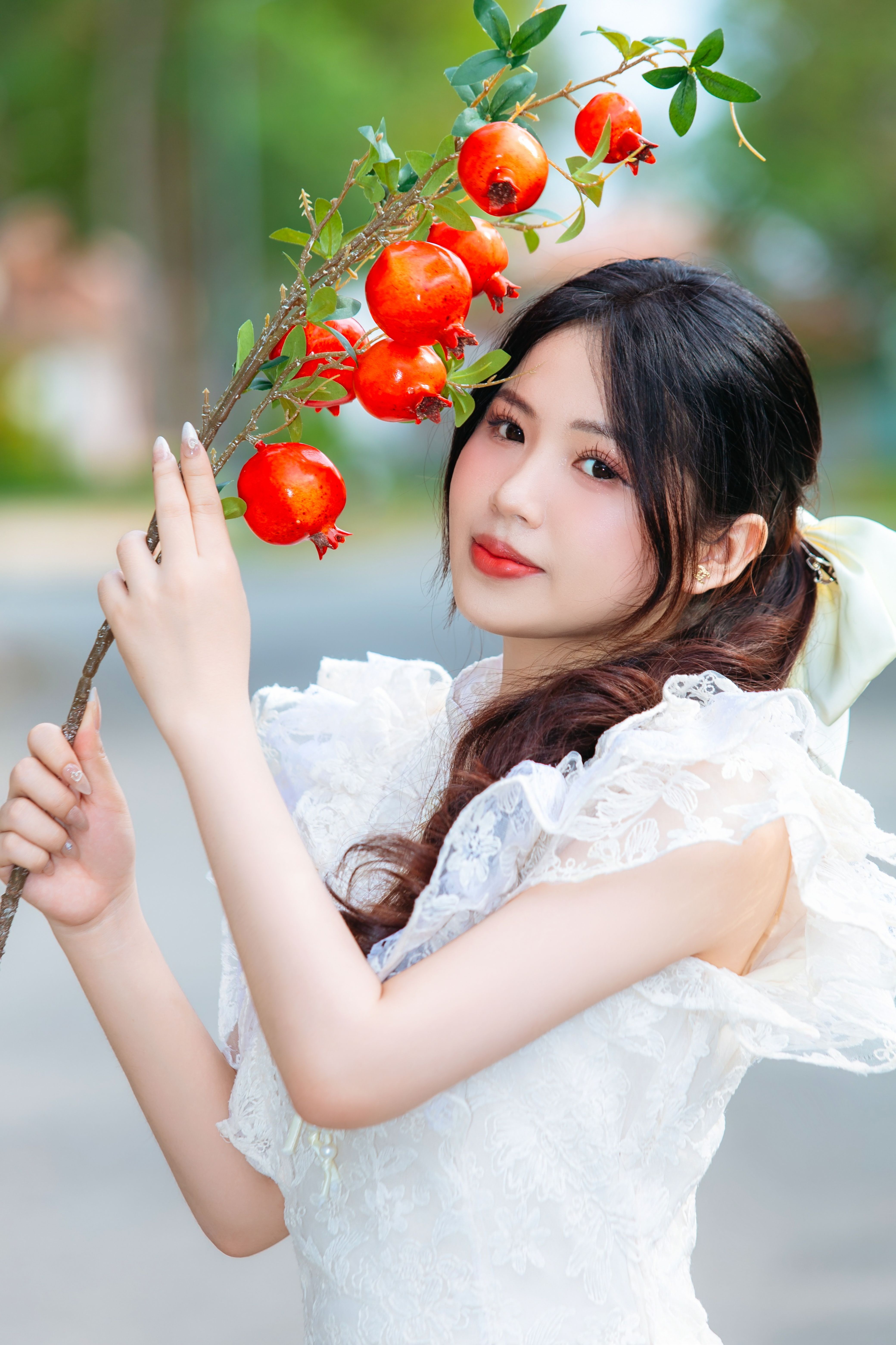 Portrait of a young woman in white holding a pomegranate branch, outdoors.