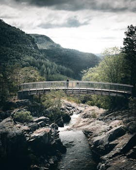 一座宁静的木桥横跨在岩石溪流之上，溪流蜿蜒于郁郁葱葱的青山之间