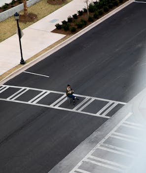A solitary figure reading a book on a city crosswalk, captured from above.