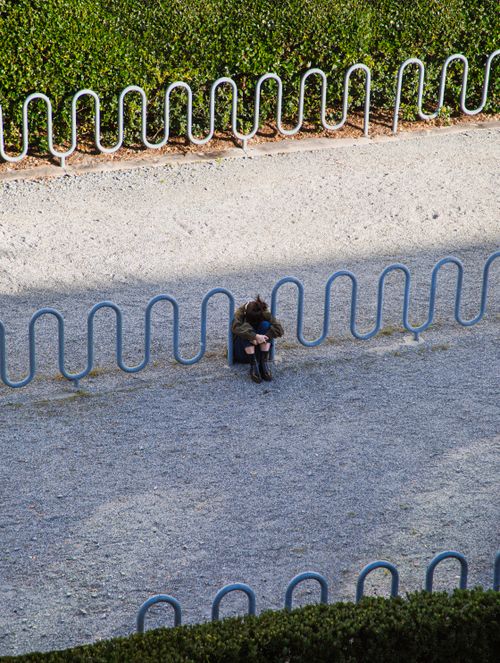 Free A lone person seated near bike racks on a gravel path, conveying solitude. Stock Photo