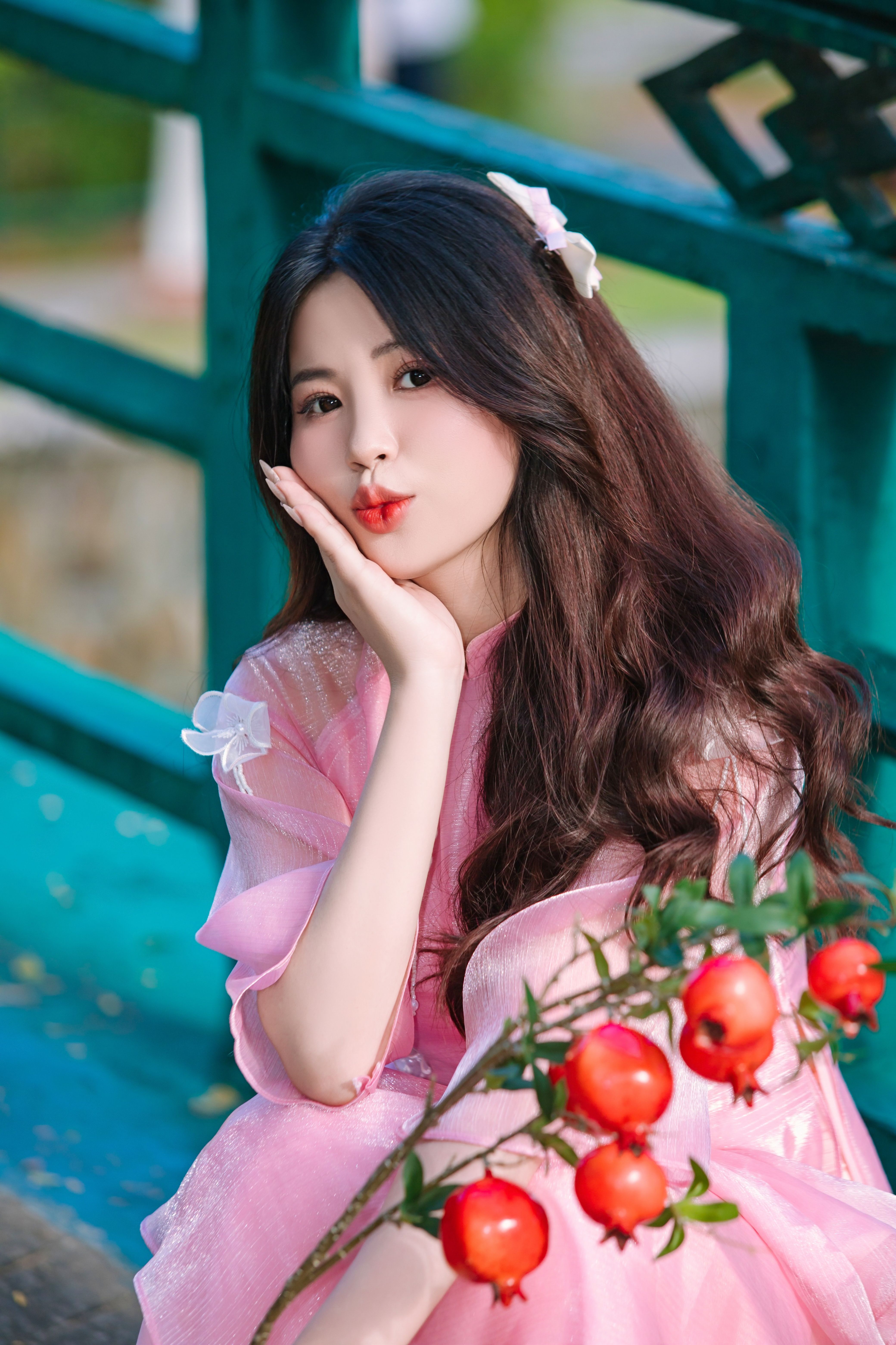 Young woman in a pink dress with long hair, holding a branch with red berries, outdoors.