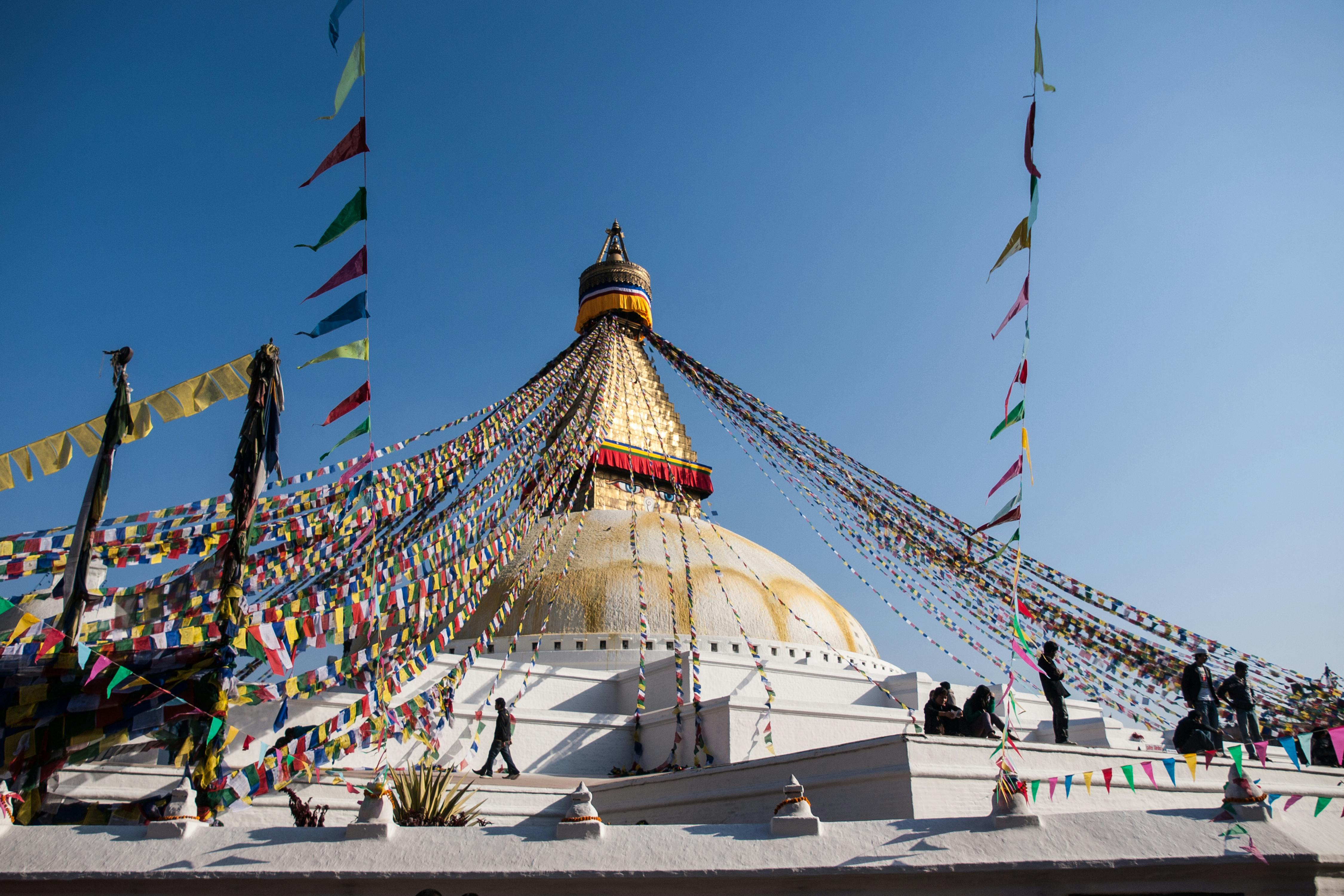 Boudhanath Stupa, adorned with colorful Tibetan prayer flags, in Kathmandu under a clear blue sky.