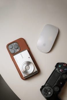 A flat lay of various tech gadgets including a camera phone, gaming controller, and wireless mouse on a white surface.