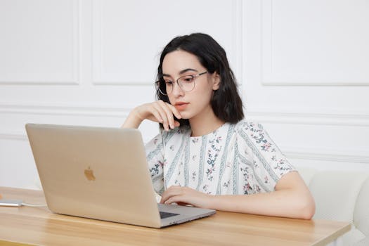 Photo by GlassesShop GS Woman in floral blouse wearing glasses, focused on laptop work at home.