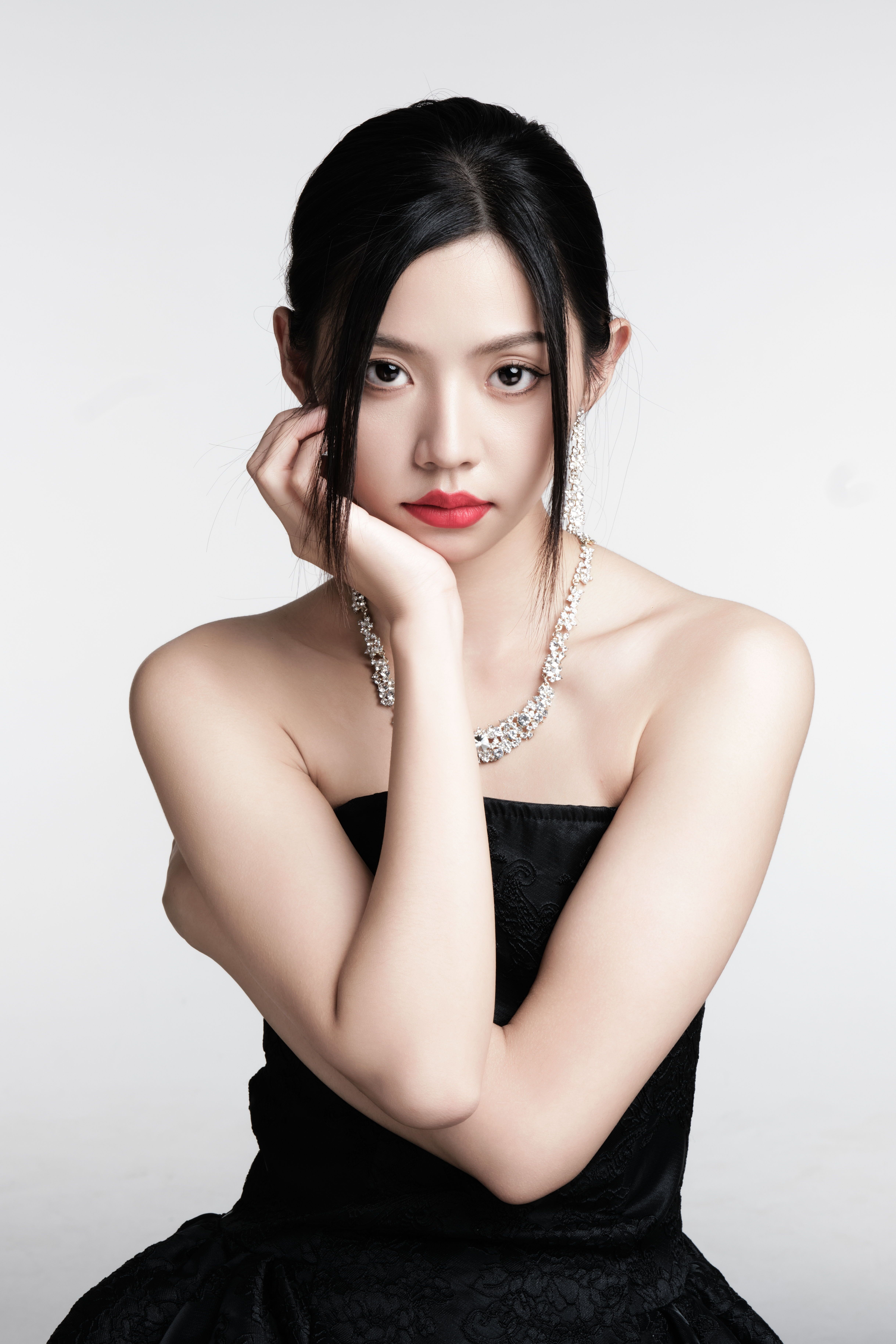 Chic portrait of a woman in a black dress and jewelry against a light background.