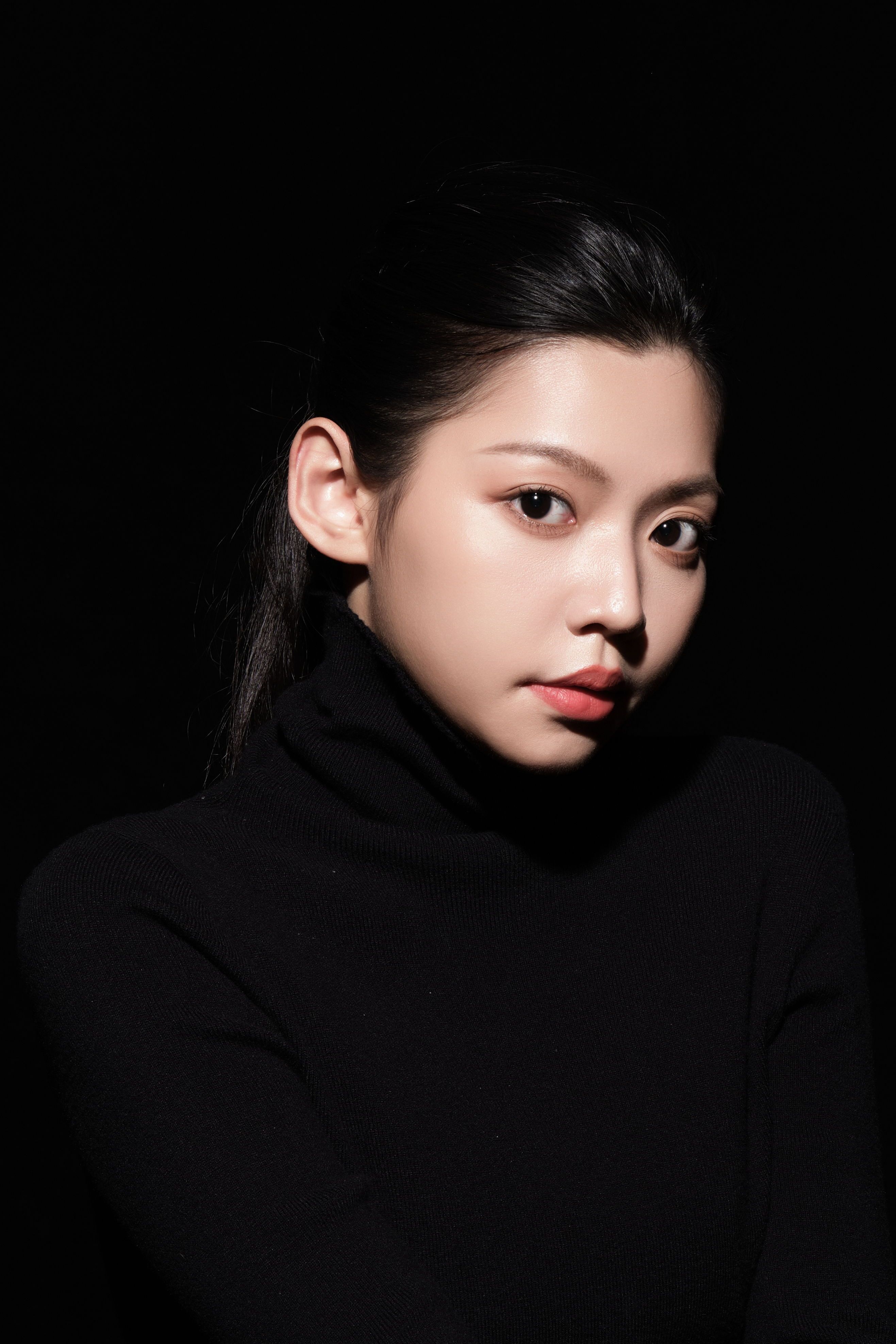 Sophisticated portrait of an Asian woman in a black turtleneck against a dark background.
