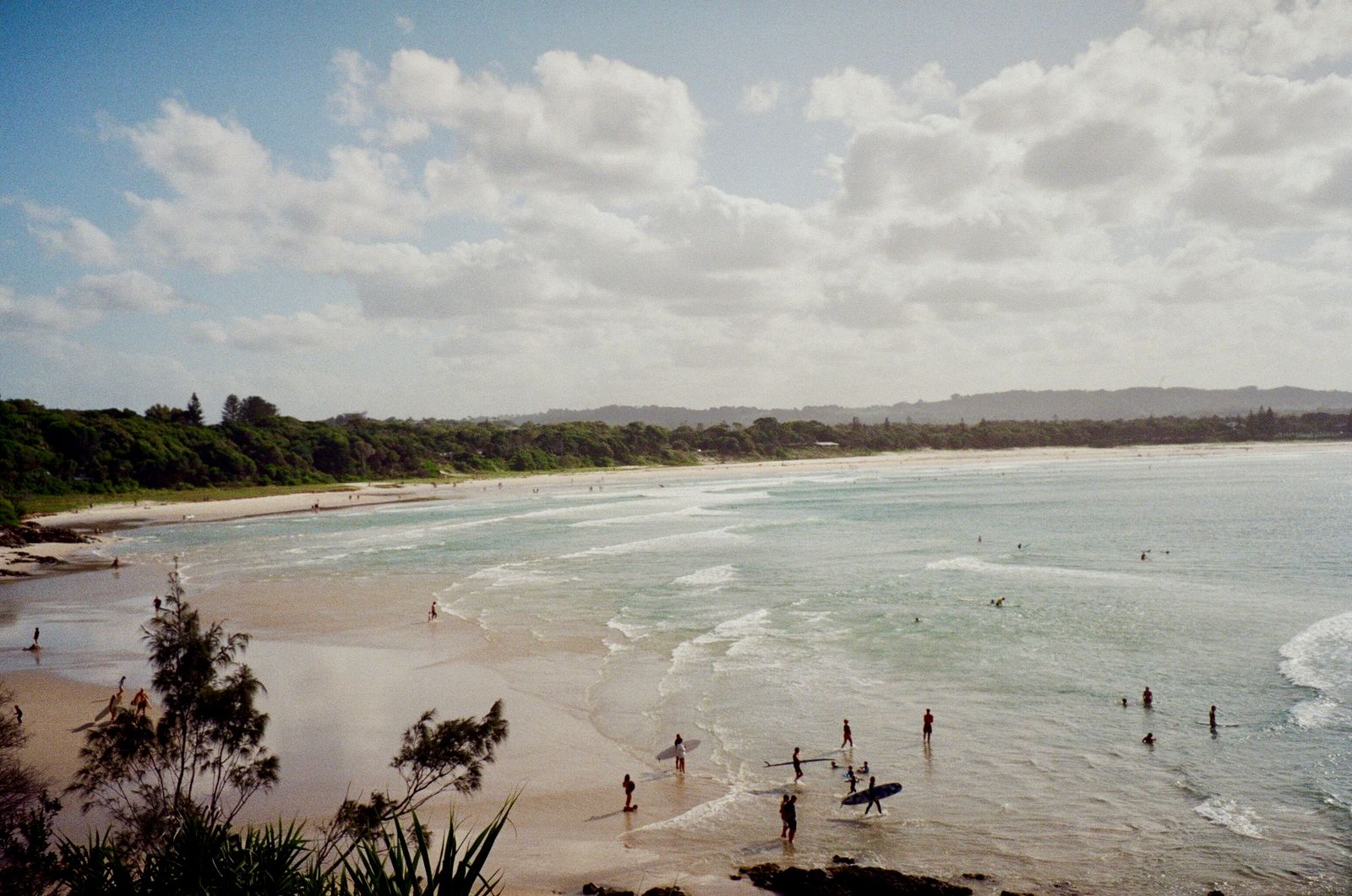 Sweeping view of Byron Bay beach with surfers and clouds at sunset