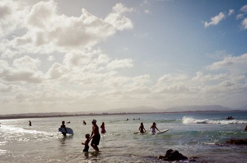 Free A lively summer day at Byron Bay, Australia, with surfers riding the waves and children playing in the water. Stock Photo