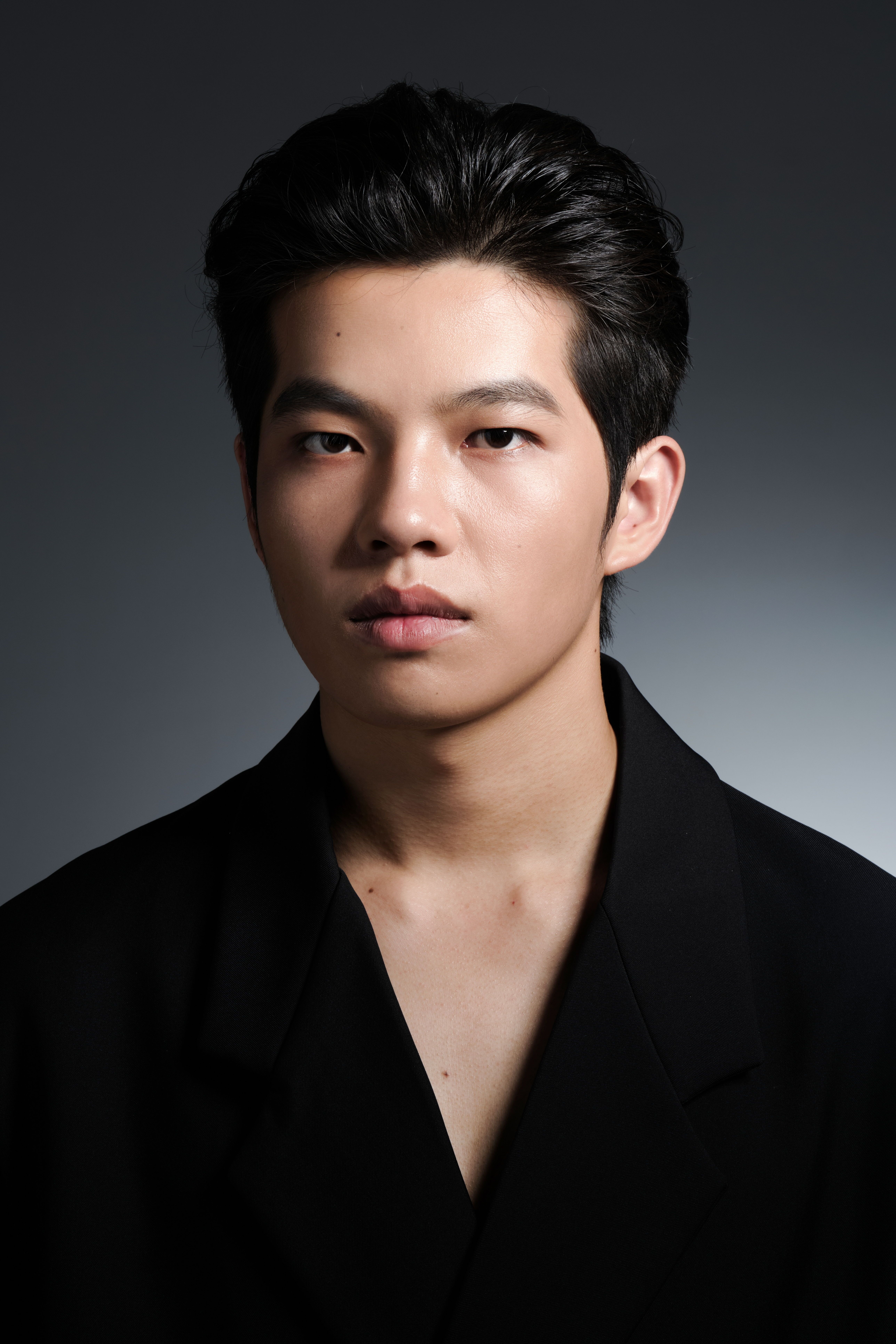 Studio portrait of a young man in a black coat with a neutral background.