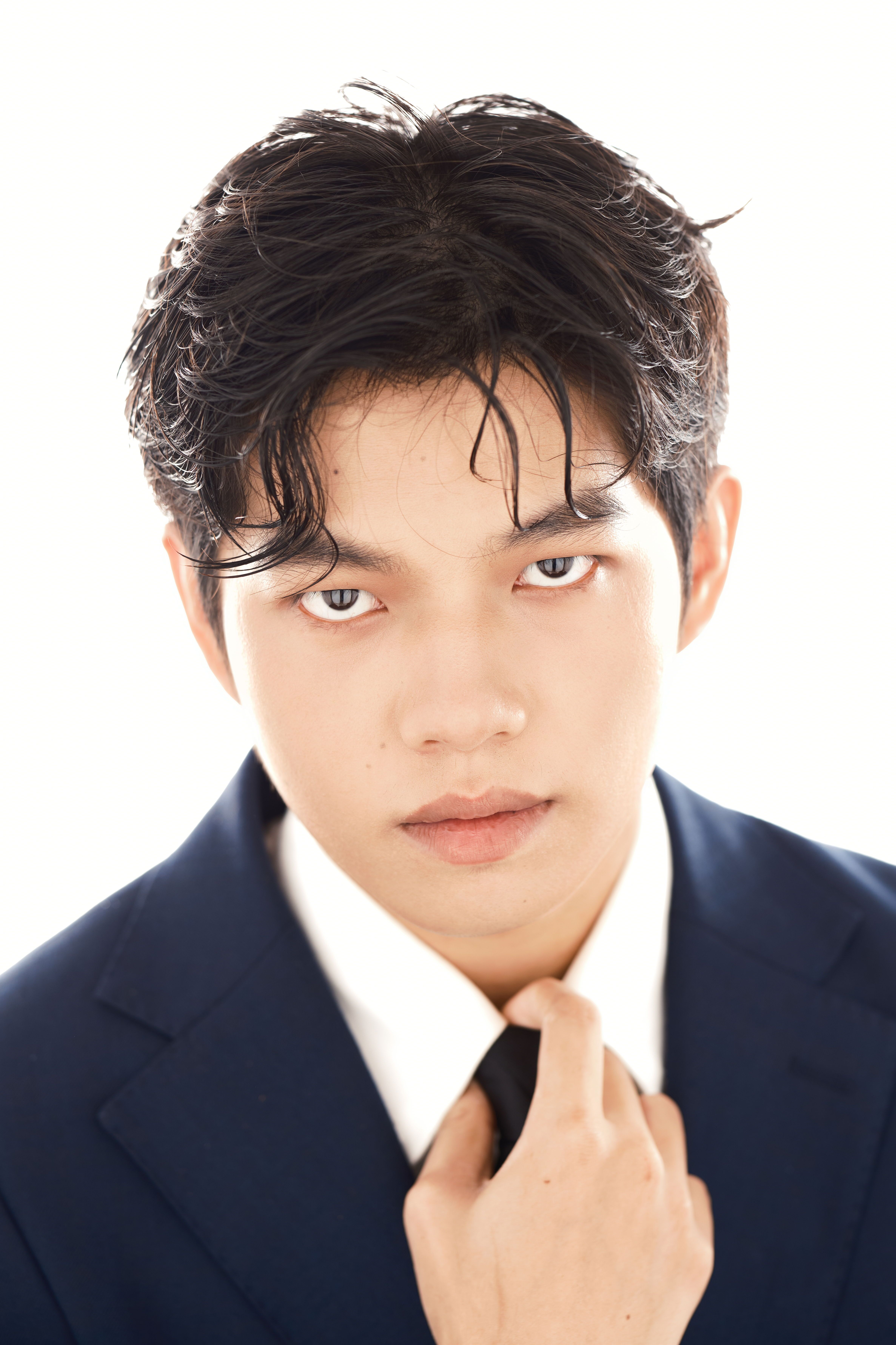Professional portrait of a young man in a suit posing confidently against a white background.